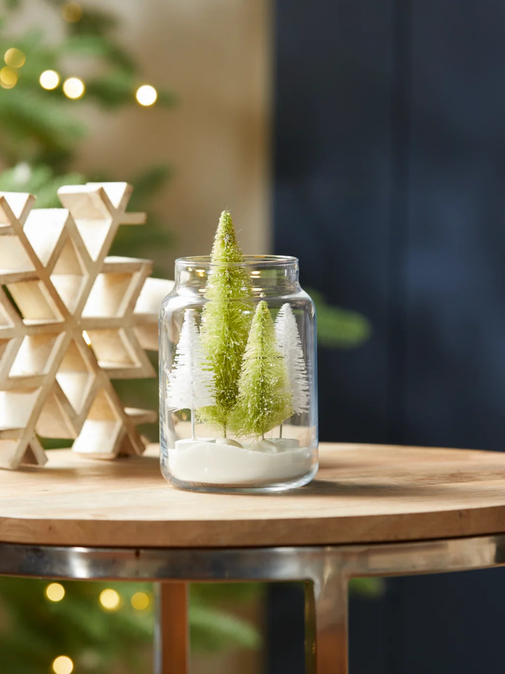 A upcycled candle jar with Christmas trees and fake snow inside the jar.